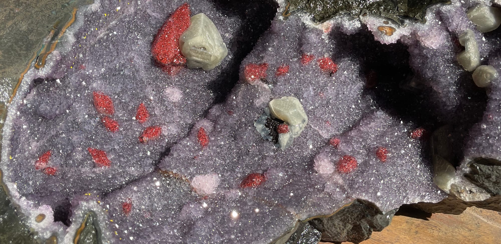A geode slab more than a meter long, open, with red calcite crystals; a hand and a tape measure give the scale