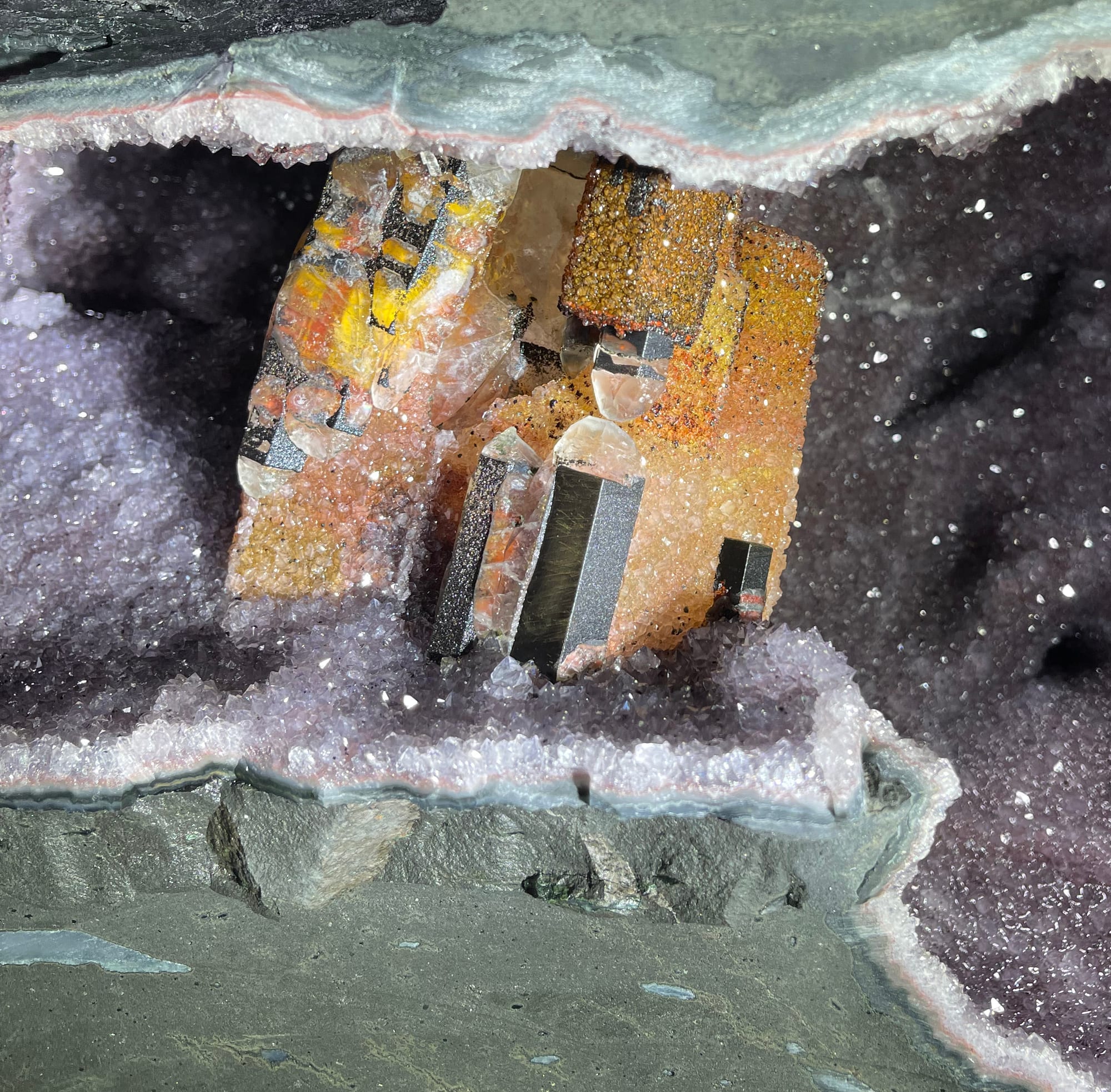 A large open geode with orange calcite crystals inside; on top, a pair of work gloves