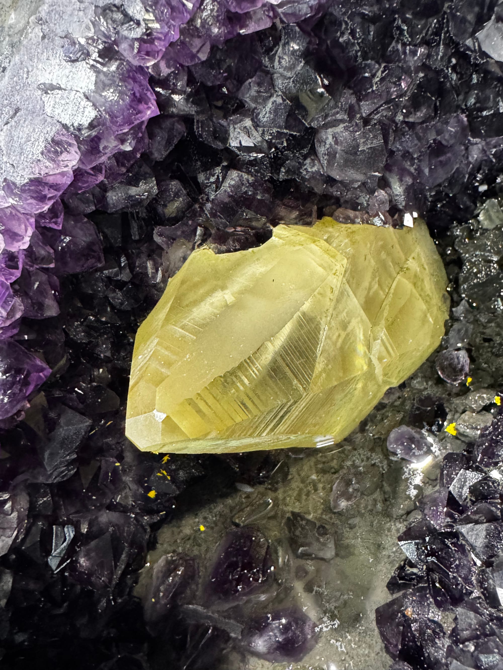 A large yellow calcite crystal inside an amethyst geode