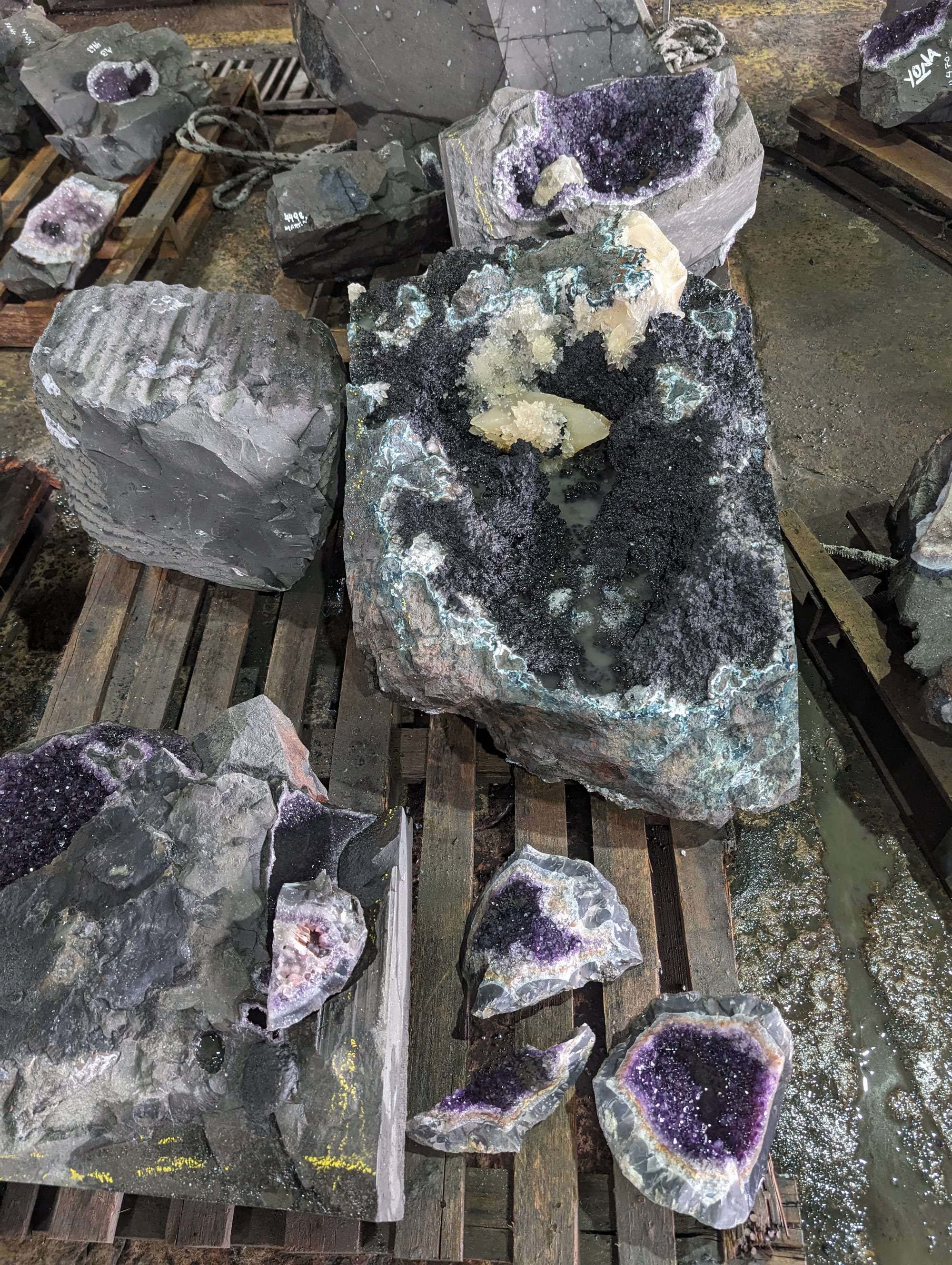 Gran geoda de amatista con calcita y bordes turquesa, rodeada de otras piedras sobre tarimas