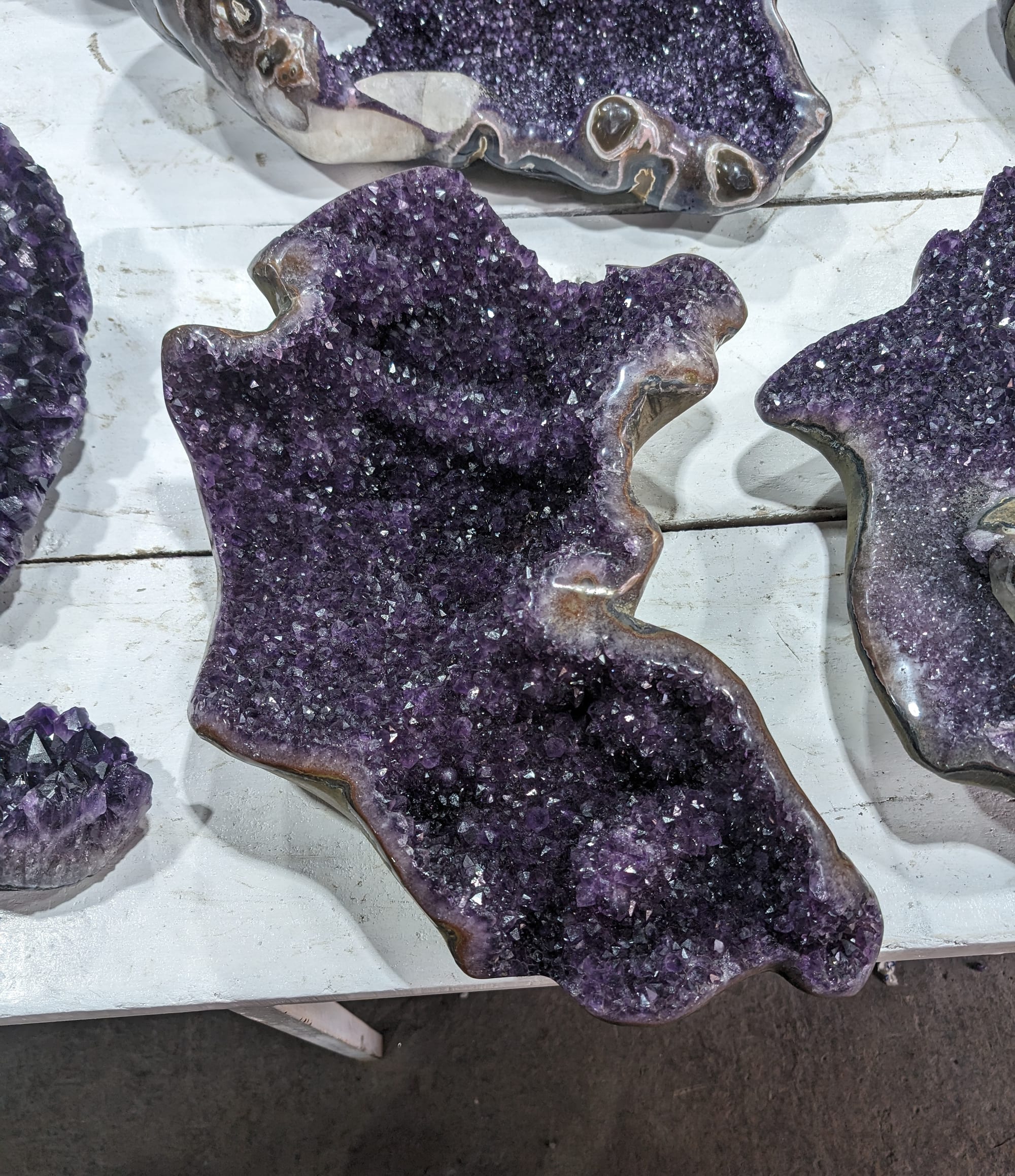 Amatista terminada en forma libre, de contorno ondulado, cubierta de cristales violetas, sobre una mesa blanca