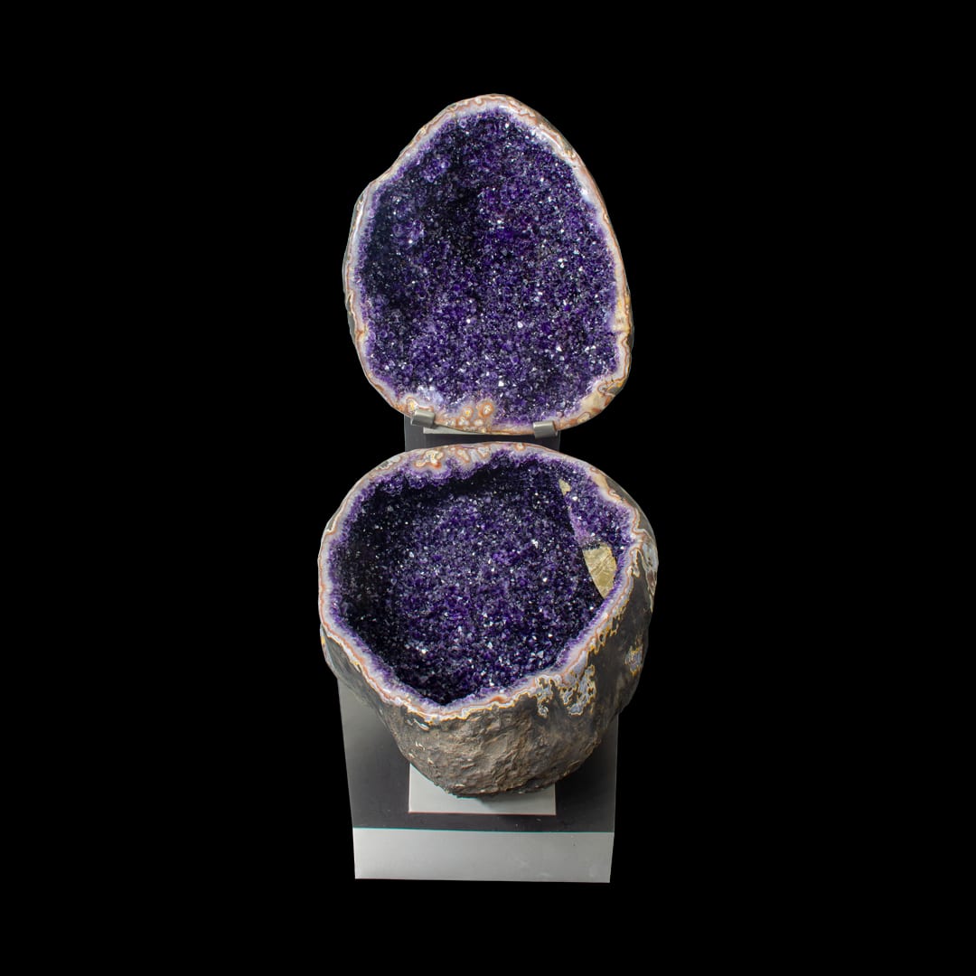 An amethyst geode opened into two halves, the top above the base, on a metal stand