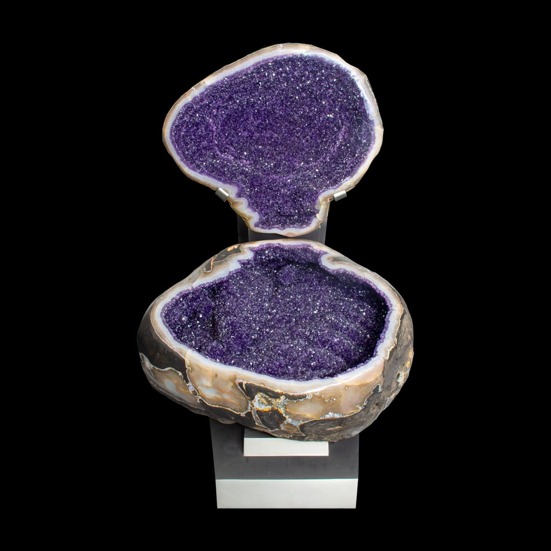 An amethyst geode opened into two halves, the top above the base, on a metal stand
