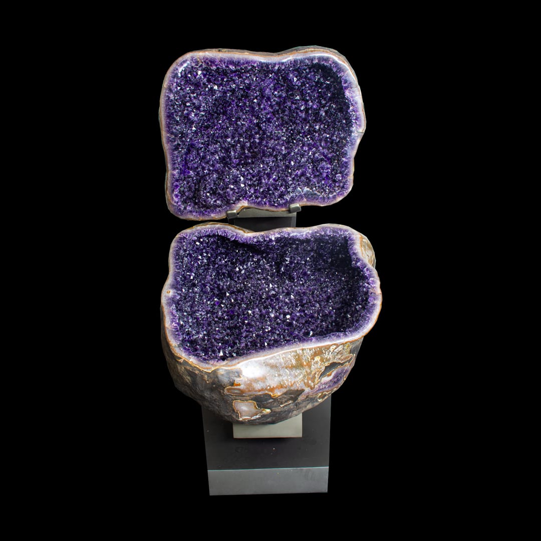 An amethyst geode opened into two halves, the top above the base, on a metal stand
