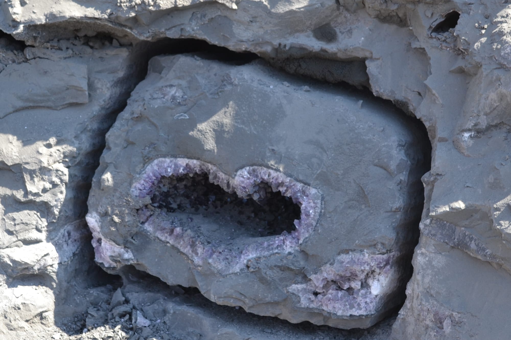 An amethyst geode still embedded in the rock of the quarry face: the block cut out and the cavity open, before extraction