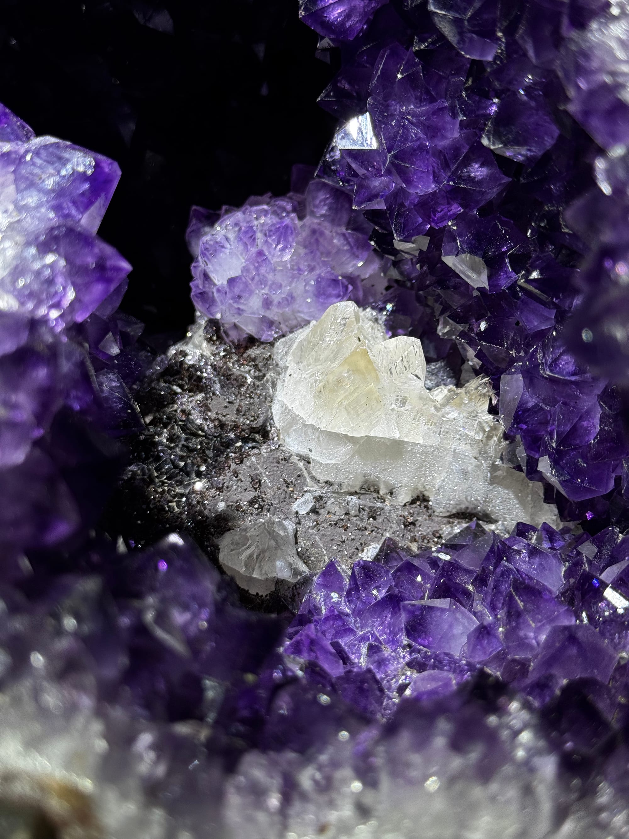 A clear white calcite crystal on a bed of dark amethyst