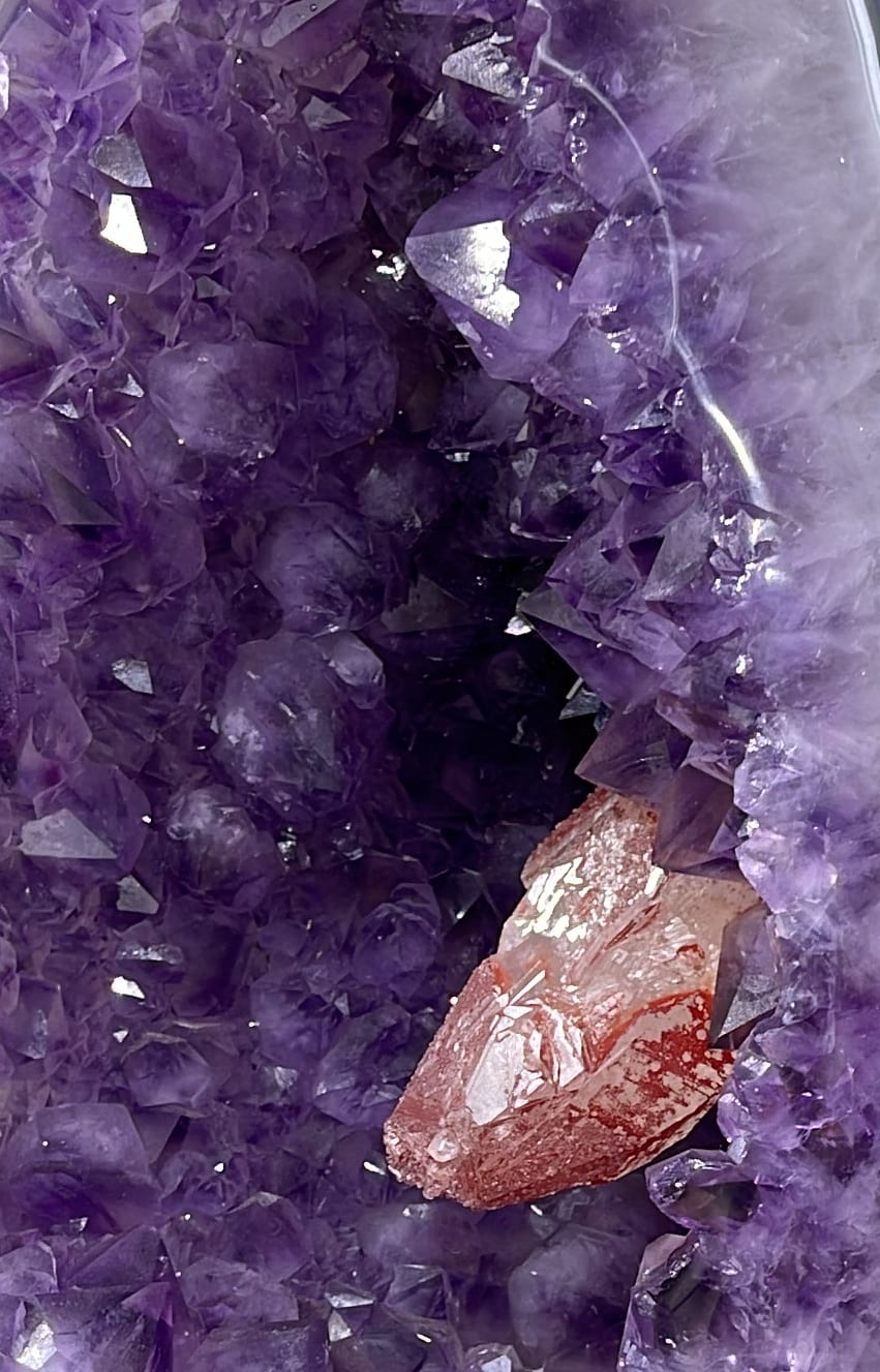 Interior de un huevo de amatista pulido, con una calcita roja entre los cristales violetas