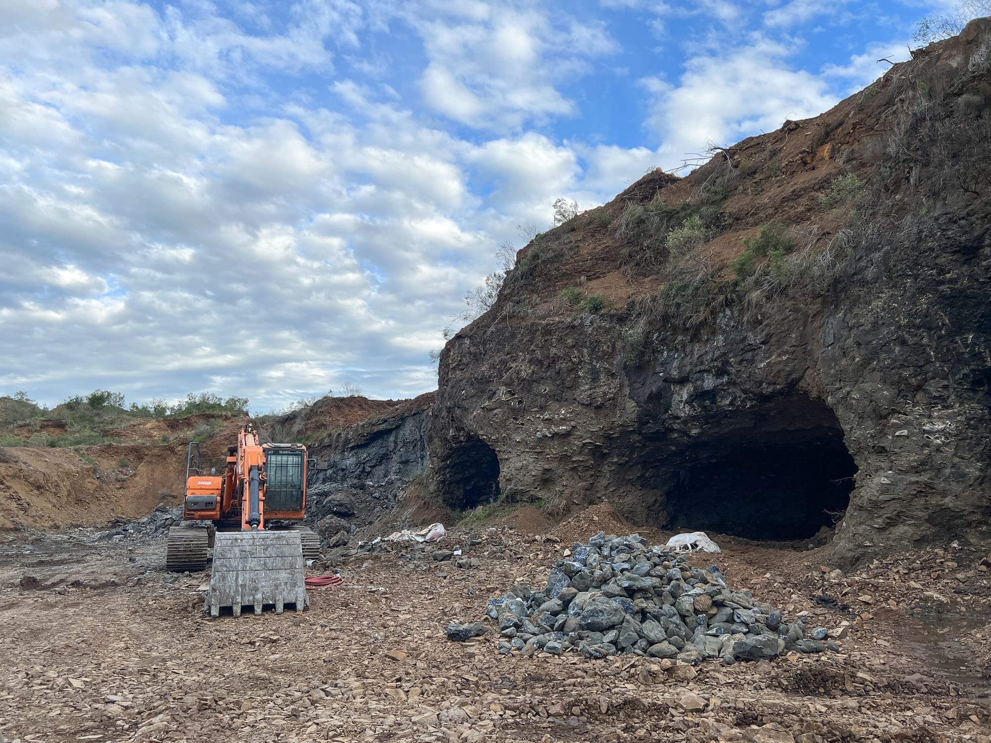 Excavadora junto a las bocas de galería abiertas en el frente de roca